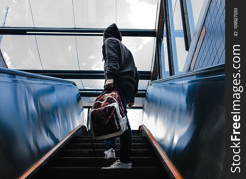 Person Wearing Black Hooded Jacket Standing on Escalator While Holding Backpack
