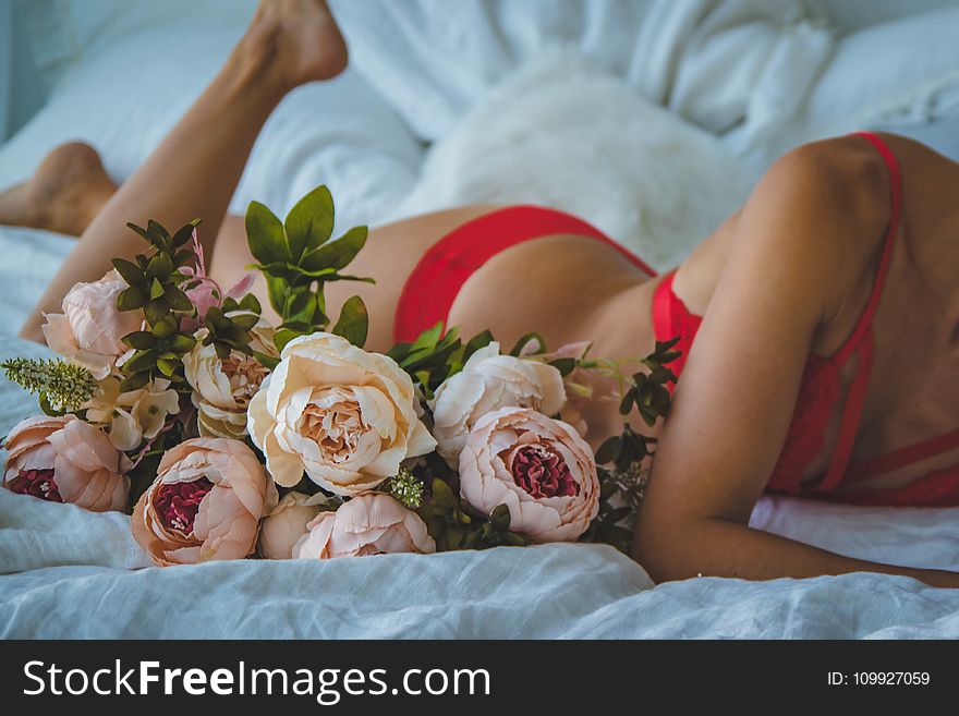 Woman In Red Two-piece Bikini Lying On Bed Beside Of White And Pink Roses