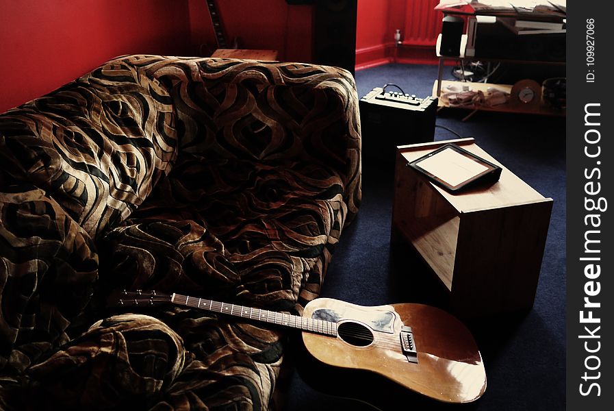Brown Acoustic Guitar Leaning on Brown Velvet Couch