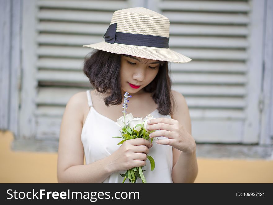 Woman Wearing Beige Sun Hat and White Sleeveless Top Holding White Flowers