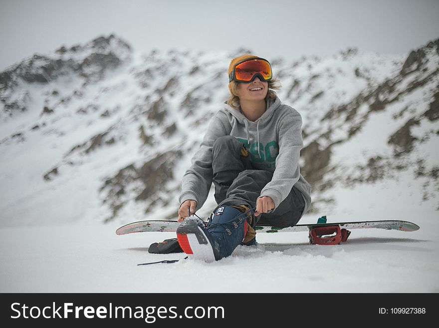 Person in Grey Hoodie Sitting on Snowboard