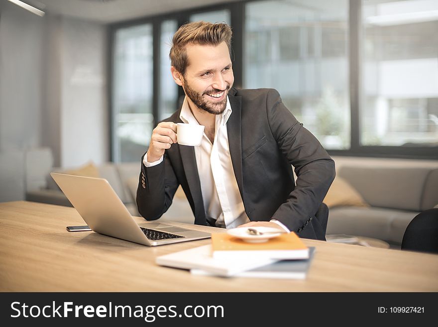 Man Holding White Teacup In Front Of Gray Laptop