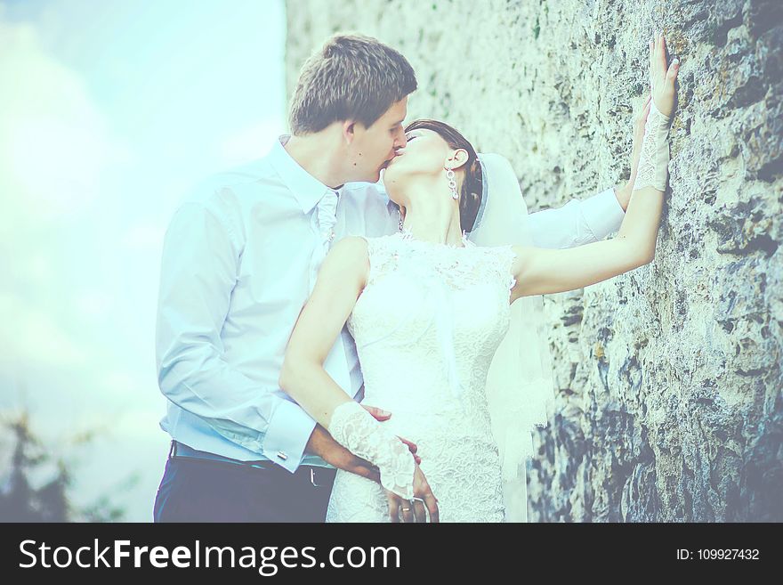 Man Kissing Woman Wearing Sleeveless Wedding Gown