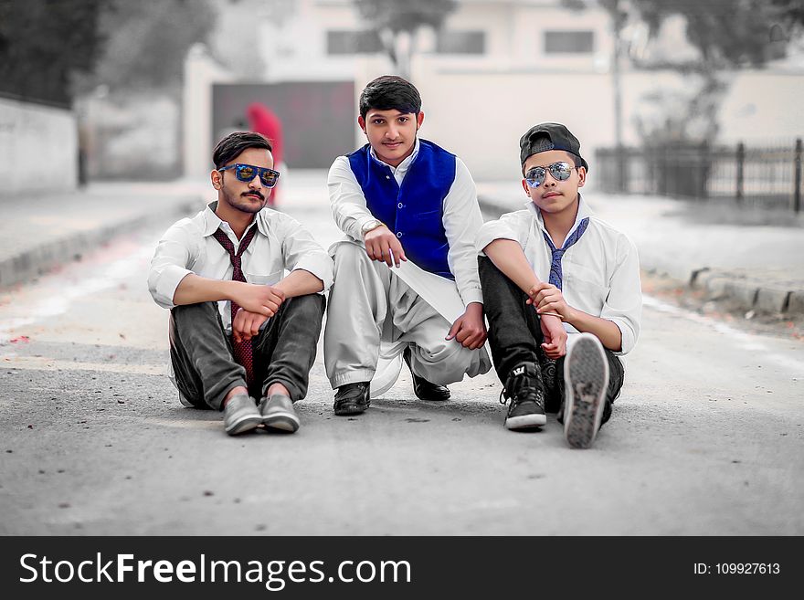 Three Men Sitting on Gray Concrete Road