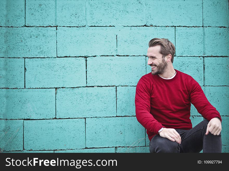 Man Wearing Red Sweatshirt and Black Pants Leaning on the Wall