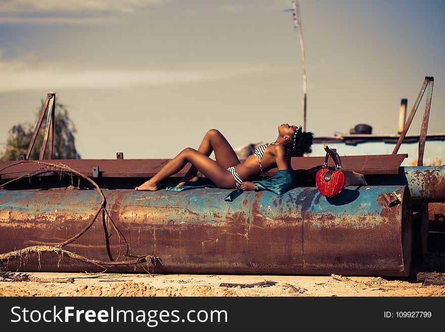 Woman in White and Blue Striped Two Piece Lying on Rustic Brown Metal Tank