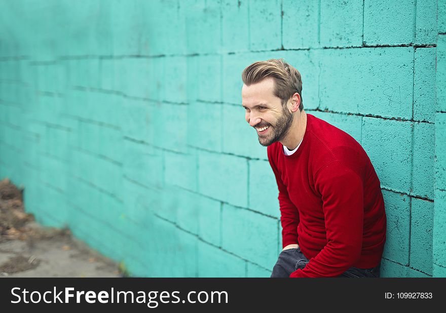 Man Wearing a Red Sweater Leaning on a Blue Wall