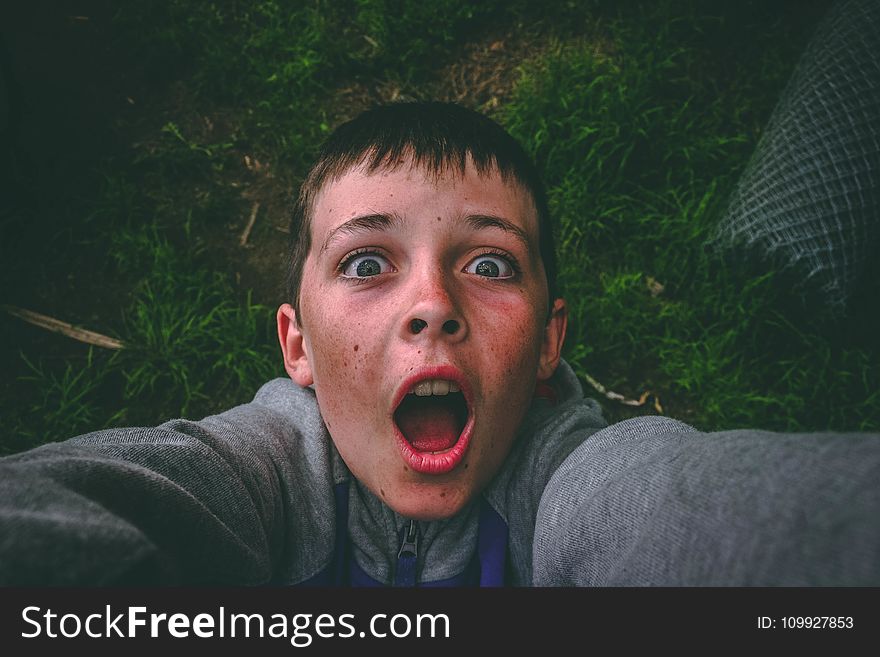 Opened Mouth Black Haired Boy in Gray Full-zip Jacket Standing on Grass Field Taking Selfie