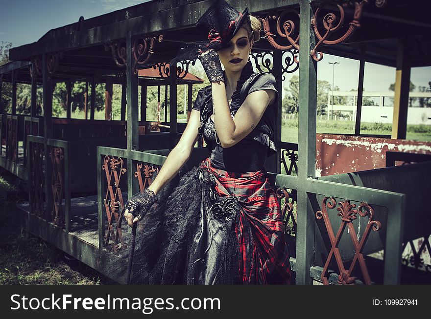 Woman in Black and Red Short-sleeved Dress Standing in Front of Green Steel Structure