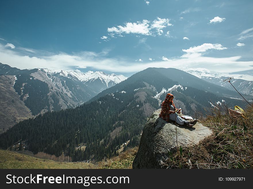 Person Sitting on Rock Near Cliff