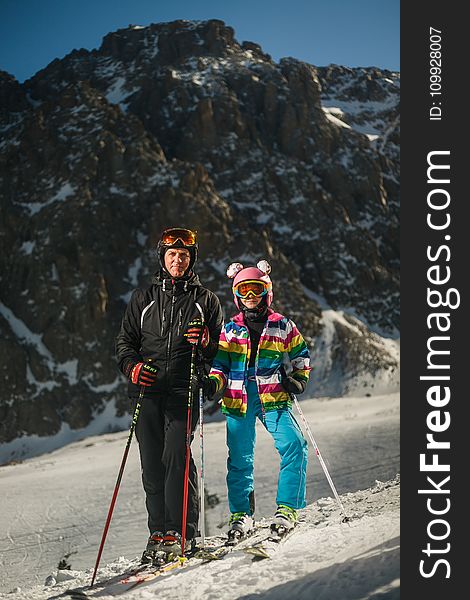 Man And Woman Wearing Snow Ski Suit And Snow Ski With Poles During Snow