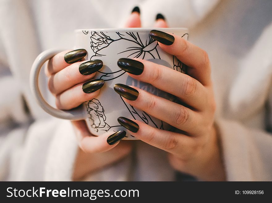 Woman With Black Manicure Holding White and Grey Floral Ceramic Cup