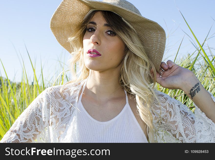 Woman Wearing Brown Hat And White Cardigan Standing In Middle Of Grass Field