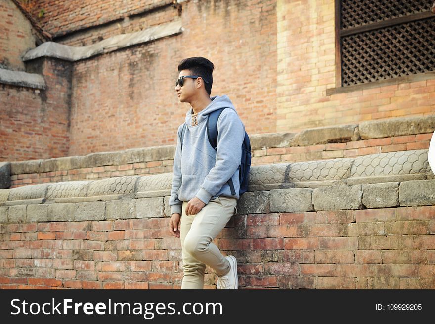 Man in Heather-grey Pullover Hoodie and Beige Pants Standing Near Brick Wall