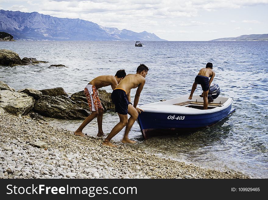 Three Men Pushing Speed Boat on Seashore