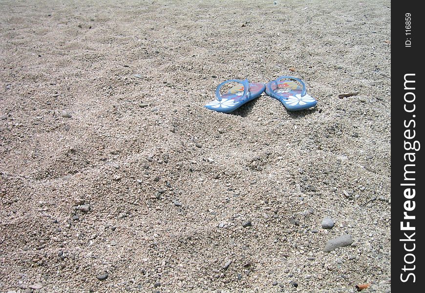 A pair of flip flops on the sand.