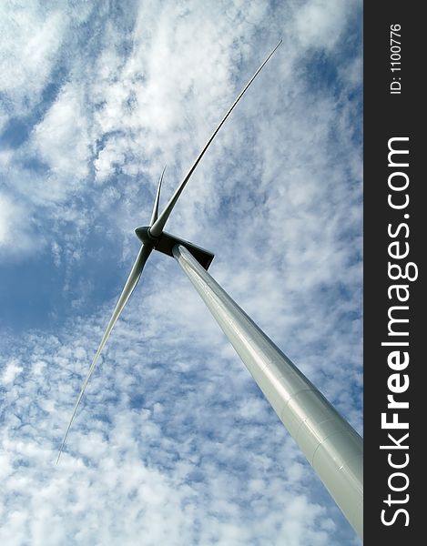 Looking up at a wind turbine set against a blue sky and clounds. Looking up at a wind turbine set against a blue sky and clounds