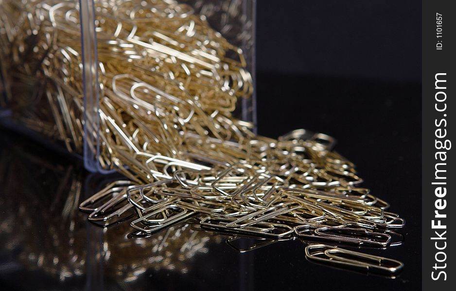 Box of gold paperclips on black background
