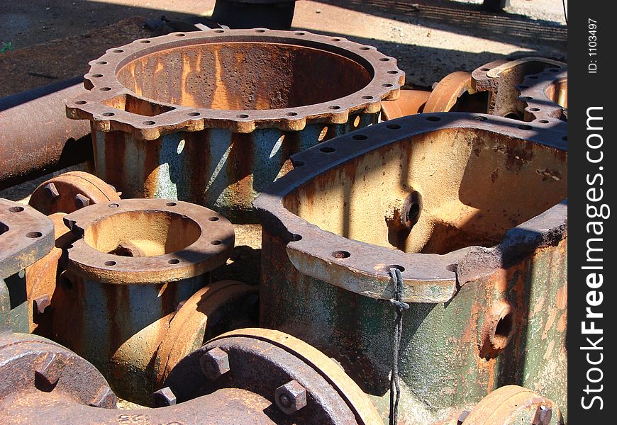 Pieces of old machinery which are rusted and have turned shades of orange, brown, and green and black. They are in the sunlight and there are dramatic shadows and highlights. Pieces of old machinery which are rusted and have turned shades of orange, brown, and green and black. They are in the sunlight and there are dramatic shadows and highlights.
