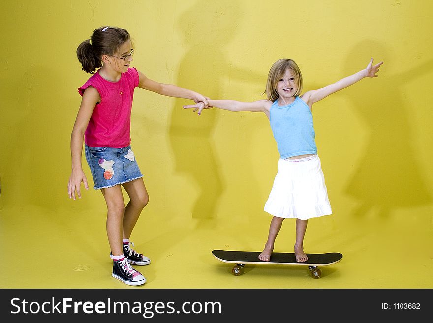 An older girl pulling her sister on a skateboard. An older girl pulling her sister on a skateboard