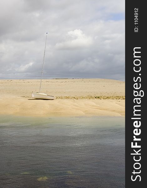 Yacht on remote island. Golden sands and blue seas under moody sky.