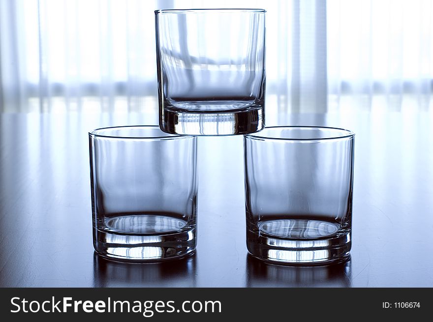 Three glass tumblers stacked in a pyramid against a backlit window. Three glass tumblers stacked in a pyramid against a backlit window
