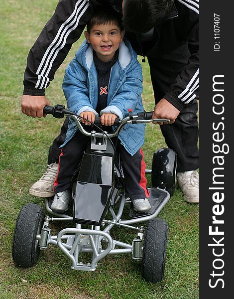 Little boy on a mini moto quad bike with an adult holding the handlebars and guiding the bike. Little boy on a mini moto quad bike with an adult holding the handlebars and guiding the bike.