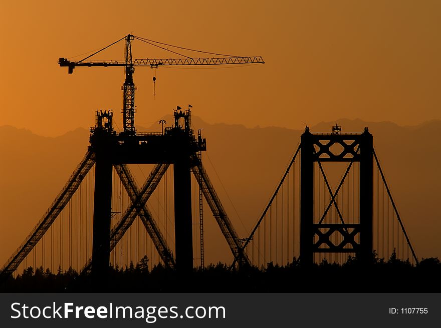 Sunset behind Tacoma Narrows Bridge (old and new bridges) with Olympic Mountains, with crane on new bridge. Sunset behind Tacoma Narrows Bridge (old and new bridges) with Olympic Mountains, with crane on new bridge