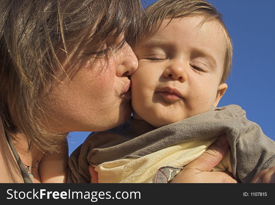 Mother kissing her son on blue sky. Mother kissing her son on blue sky