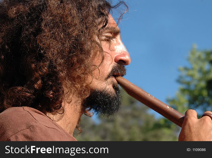 Men with long hippie hair playing the flute under a blue sky. Men with long hippie hair playing the flute under a blue sky