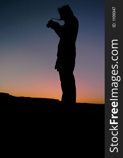 Silhouette female photographer at sunset taking pictures on a digital slr