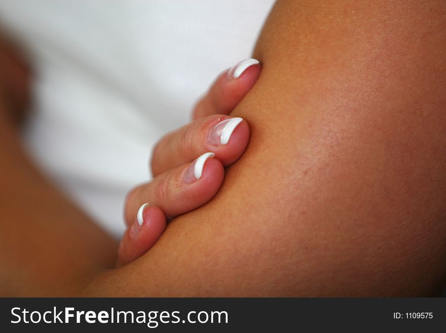 Young woman in white top with her arms folded, cropped shot from the left side focus on the four visible fingers resting on her left arm. Young woman in white top with her arms folded, cropped shot from the left side focus on the four visible fingers resting on her left arm.