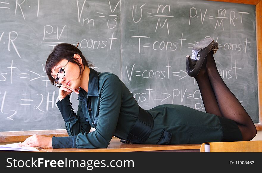 Beautiful student lays on a school desk near a blackboard