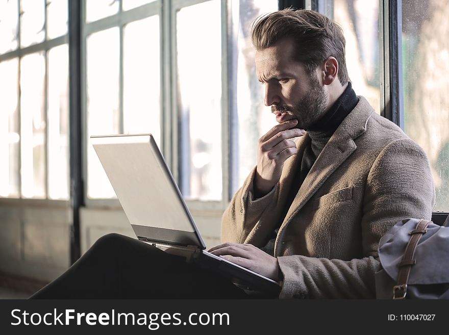 Man Wearing Brown Jacket and Using Grey Laptop