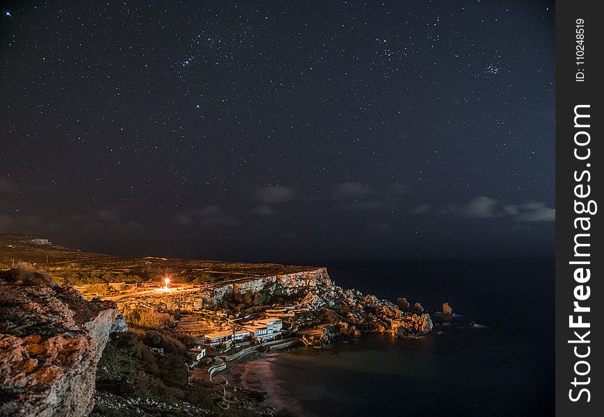 Rock Cliff Near Body of Water Under Clouds and Sky during Nighttime