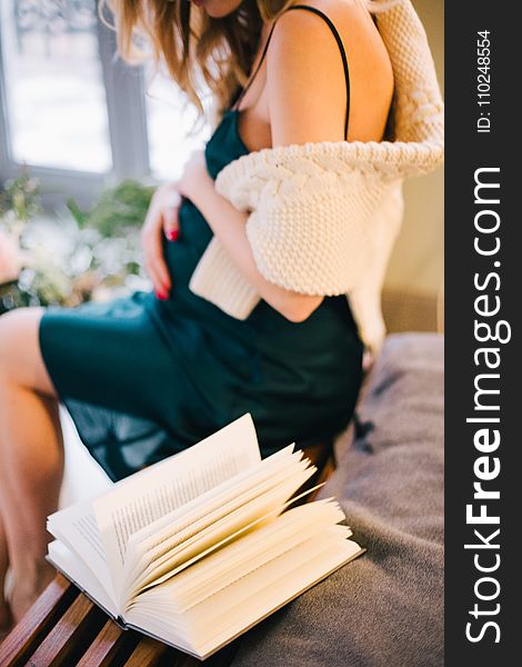 Selective Focus of Pregnant Woman in Black Spaghetti Strap Dress Sitting on Chair Beside Opened Book