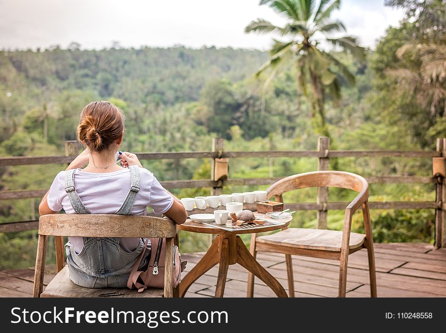 Brown-haired Woman Sitting on Brown Wooden Chair on Patio