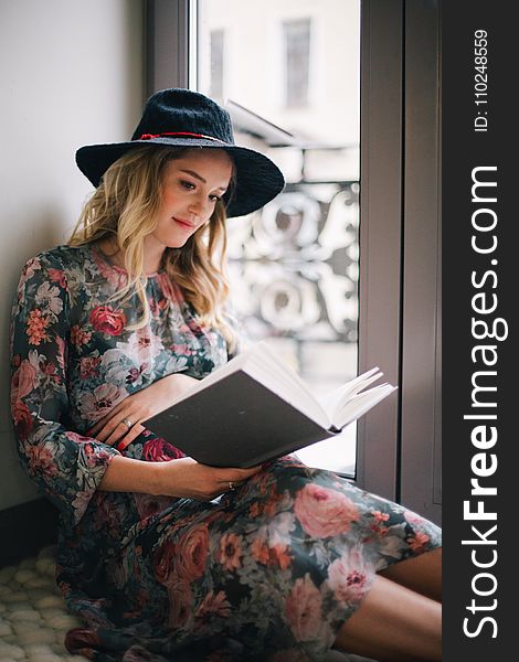 Pregnant Woman Wearing Green, Red, and White Floral Dress Reading a Book Near Window