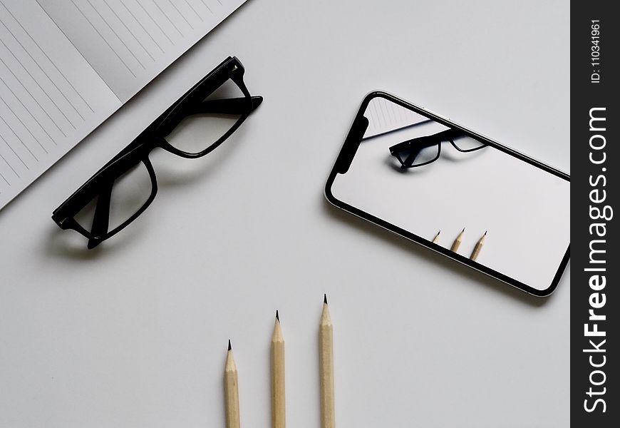 Three Pencils, Eyeglasses, And Smartphone On White Table