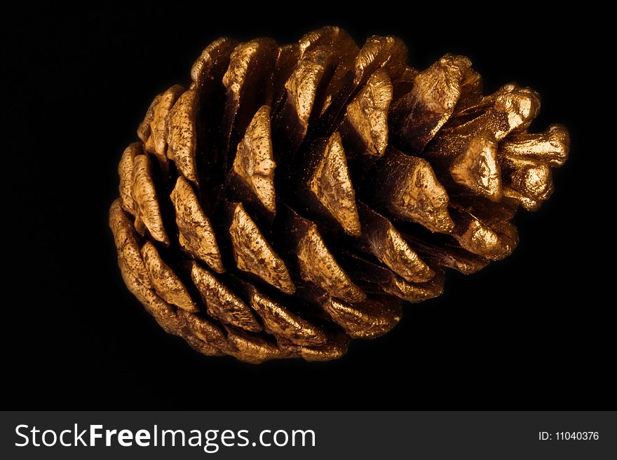 A close-up of a gold painted pine cone against a black background. A close-up of a gold painted pine cone against a black background.