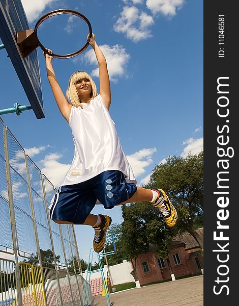 Young blond girl is playing basketball outside, hanging on a basketball shield. Young blond girl is playing basketball outside, hanging on a basketball shield