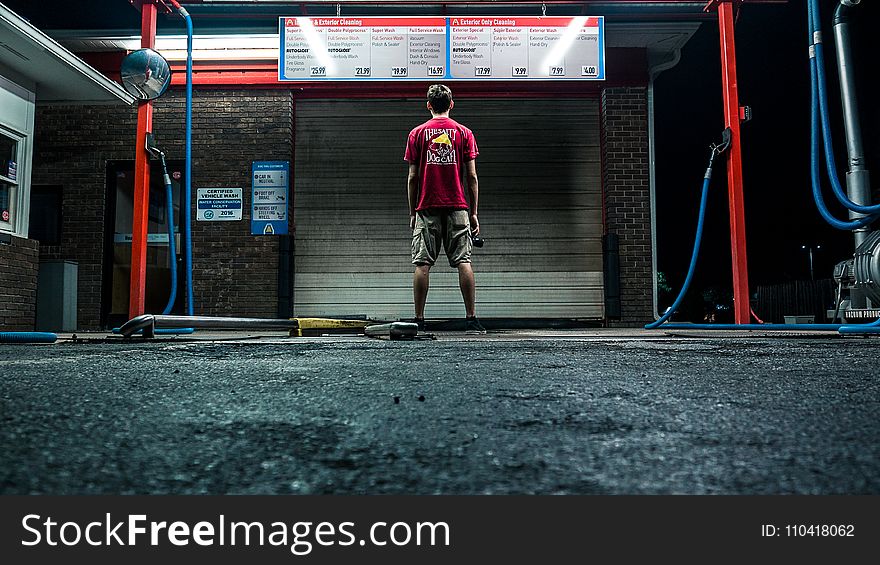 Man In Red Shirt And Brown Shorts Standing Near Wall