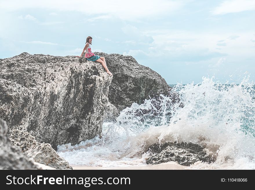 Woman Sitting Of Rock Near Body Of Water