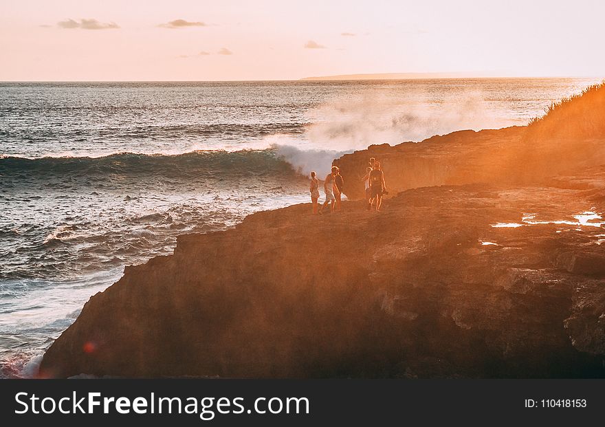 People Standing on Cliff Near Body of Water Golden Hour Photography