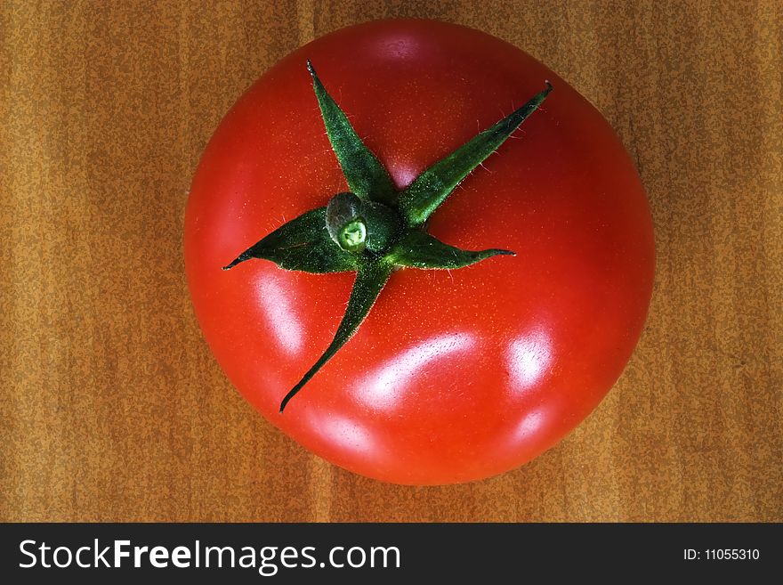 A single red tomatoe on a brown  wooden background