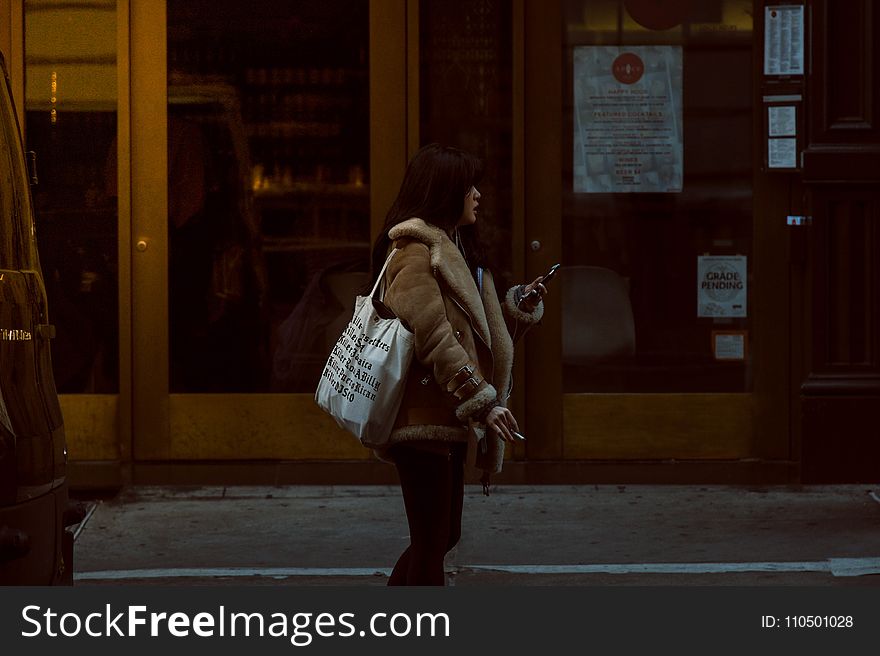 Woman Carrying White Tote Standing Beside Brown Glass Door Building