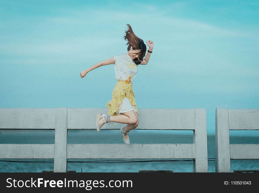 Jumpshot Photography Of Woman In White And Yellow Dress Near Body Of Water