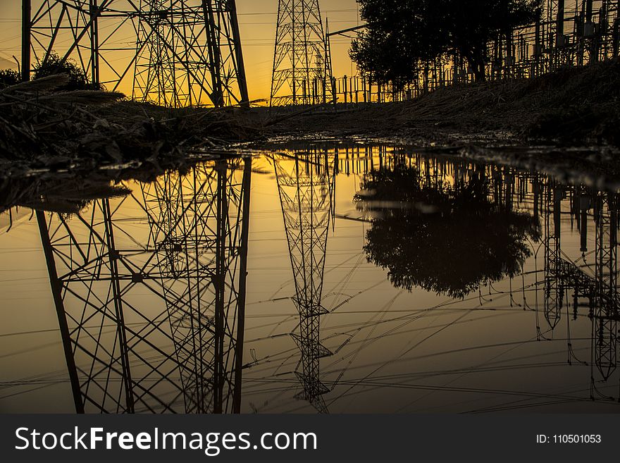 Silhouette of Trees and Electric Tower Reflecting on Body of Water during Sunset