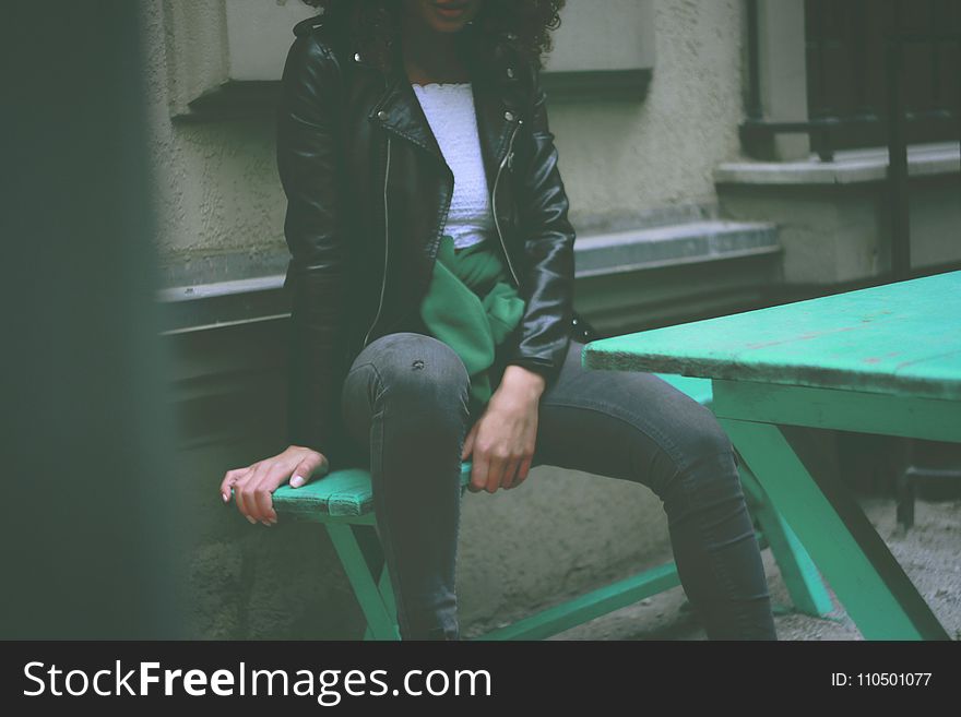 Woman Wearing Black Leather Jacket Sitting On Green Wooden Bench