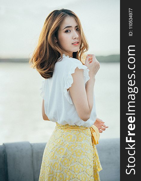 Photo of Woman Wearing White Sleeveless Shirt and Yellow Floral Skirt Near Body of Water